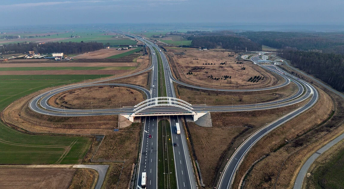 Węzeł A2 Łyszkowice · realna geografia, która stała się znakiem marki Widok z lotu ptaka na węzeł autostrady A2 Łyszkowice — dwa łukowate zjazdy łączące się w centralnym punkcie skrzyżowania, otoczone polami uprawnymi